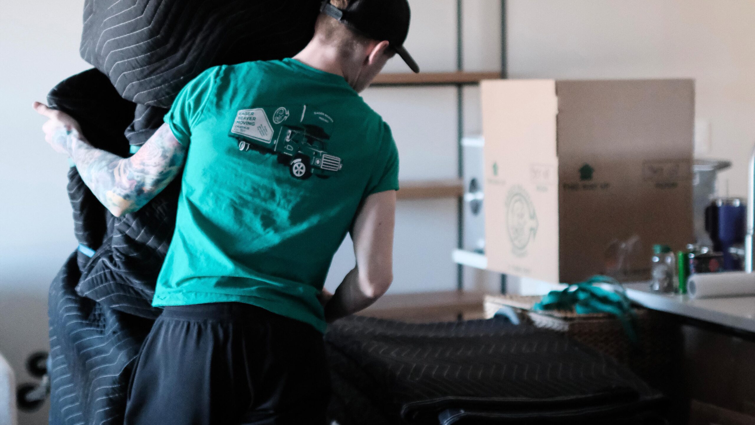 An Eager Beaver mover in a green shirt carefully carrying wrapped furniture during a home move